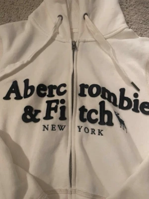 Vit hoodie från Abercrombie & Fitch - Vit zip-hoodie från Abercrombie & Fitch i storlek L. Litet slitage på båda ärmarna, se sista bild.