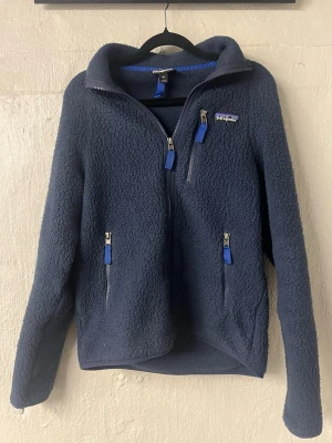 Mörkblå flecce från Patagonia - Mysig mörkblå teddyjacka från Patagonia med dragkedja framtill och tre fickor med blå detaljer. Passar någon perfekt som är ca 160-170 cm lång. Pris kan diskuteras!
