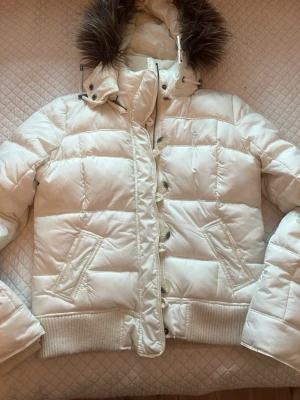 Vit dunjacka från Abercrombie & Fitch - Snygg vintage vit dunjacka från Abercrombie & Fitch med avtagbar huva och fuskpäls. Köpt begagnad från vinted för 2000kr men passade inte, säljer också för 2000kr men priset går därmed att diskuteras. Den har lite fläckar och i stl L. ÄR OCKSÅ VILLIG ATT BYTA OM NÅGON HAR SAMMA JACKA I MINDRE STRL