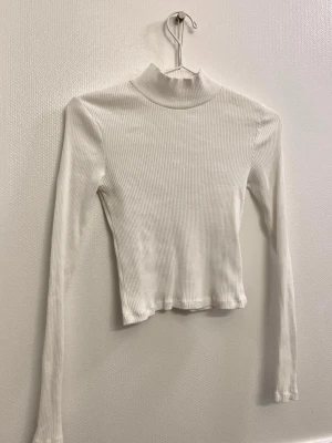 Vit polotopp - Vit ribbad polotopp med lång ärm. Toppen har en hög krage och är tillverkad i ett mjukt, stretchigt material.