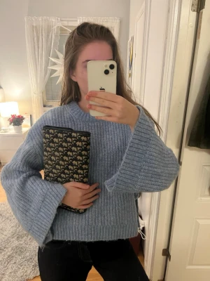 Ljusblå stickad tröja med vida ärmar - Mysig ljusblå stickad tröja med breda, vida ärmar och ribbstickade detaljer vid ärmslut och nederkant. Tröjan har en rak passform och rund halsringning, perfekt för lager-på-lager-stil under kyliga dagar.