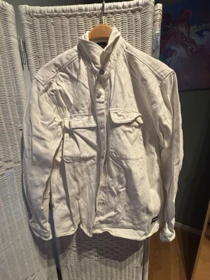 Vit overshirt från Pull&Bear - Stilren vit overshirt från Patagonia med två stora bröstfickor och knappar framtill. Tillverkad i kraftig bomull och har en hög krage. Perfekt att bära som lager över en t-shirt eller hoodie.