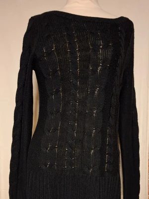 Svart kabelstickad tröja. JC - Snygg svart kabelstickad tröja med lång ärm och bred ribbad mudd vid ärmslut och nederkant. Tröjan har ett figurnära snitt och ett klassiskt flätmönster framtill. Perfekt till höst och vinter för en stilren look.