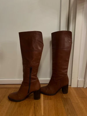 Bruna höga stövlar med klack - Snygga bruna stövlar i skinn med rund tå och stabil klack, super snygga!!