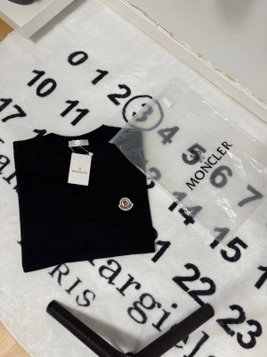 Svart Moncler t-shirt med logga - Snygg svart t-shirt från Moncler med klassisk rund hals och Monclers ikoniska logga broderad på bröstet. Tillverkad i mjuk bomull och har en clean, stilren look som passar perfekt till jeans eller shorts.