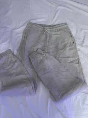 Grå mjukisbyxor från KappAhl - Snygga och bekväma grå mjukisbyxor från KappAhl med resår och snörning i midjan. Byxorna har sidofickor och är gjorda i mjukt material med borstad insida för extra komfort. Perfekta för chill eller träning.