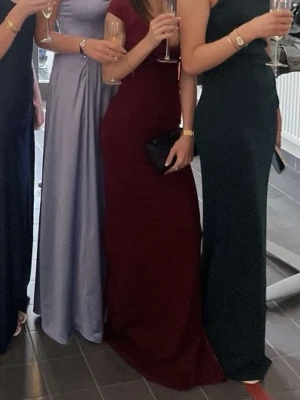 Vinröd långklänning med v-ringning - Supersnygg vinröd långklänning med v-ringad omlott överdel och offshoulder-ärmar. Klänningen har figurnära passform och markerad midja, vilket ger en elegant siluett. Perfekt för bal eller fest. Materialet är mjukt och följsamt, troligtvis polyester. Klänningen ät ganska lång, storleken är xxs men frf lång för mig och jag är 1,59 lång