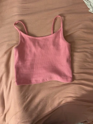 Rosa ribbad linnetopp - Säljer en ljusrosa ribbad linnetopp med smala axelband. Toppen är croppad och har en enkel, stilren design.