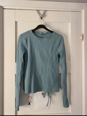 Ljusblå ribbad långärmad topp - Ljusblå långärmad topp i ribbat material med rund halsringning och dragsko i nederkanten. 