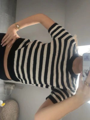 Randig croppad topp i svart och vit - Säljer en croppad topp med svart och vita ränder. Toppen har korta ärmar, rund halsringning och är gjord i ett mjukt, stickat material. Perfekt för dig som gillar en trendig och avslappnad stil.