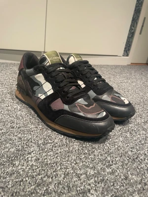 Valentino Rockrunner sneakers camouflage - Säljer ett par Valentino Rockrunner sneakers med svart, grått och vinrött kamouflagemönster. Skorna har snörning, detaljer i skinn och mocka samt nitar på hälen. Snygg kontrast mellan material och färger för en unik look. Priset är inte hugget i sten och har ni frågor är det bara att skriva☺️