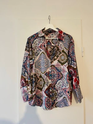 Mönstrad skjorta från Zara - Bohemisk skjorta från Zara med flerfärgat paisleymönster. Skjortan har klassisk krage och långa ärmar, perfekt för dig som gillar att sticka ut med din stil och perfekt för vårlooken. Tillverkad i polyester och har en följsam struktur som ger den där perfekta flowiga känslan.