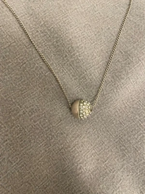 Pilgrim halsband silverklot - Säljer detta eleganta halsband i silver från Pilgrim som har ett klotformat runt hänge dekorerat med glittrande stenar på ena halvan. Kedjan är i silver och kan justeras i fyra olika längder, 38-41-44-47 cm. Perfekt att stylea med flera olika halsaband, eller bäras själv. Vissa stenar har trillat av, men det märks inte när den är på.