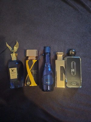 Fem exklusiva herrparfymer mix - Säljer ett set med fem snygga herrparfymer i olika blå och svarta flaskor. Märkena inkluderar TASMEEM, EXOTIC, ARIS och ARMAF. Flaskorna har unika former, detaljer i guld och silver samt eleganta lock. Perfekt för dig som gillar stilrena och lyxiga dofter.