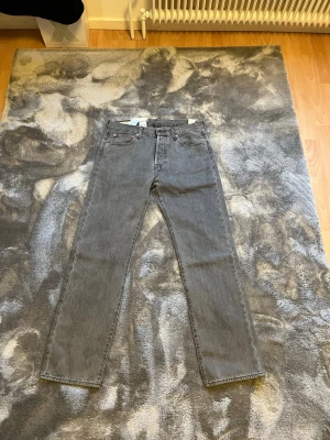 Levi's 501 grå jeans straight fit - Klassiska grå Levi's 501 jeans med rak passform och fem fickor. Jeansen har knappgylf och är tillverkade i slitstark bomullsdenim. Perfekta för dig som gillar en tidlös och clean look.