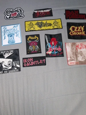 Samling tygmärken med metalband - Säljer en samling tygmärken med motiv från olika metalband som Iron Maiden, Ozzy Osbourne, Saxon och fler. Märkena har olika former, färger och tryck, perfekta att sy fast på jackor eller väskor för en personlig stil.