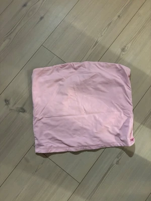 Ljusrosa bandeau tubtopp - Säljer en enkel och stilren ljusrosa bandeau tubtopp. Toppen är axelbandslös och har en mjuk, stretchig passform som sitter skönt mot kroppen. Perfekt att matcha med jeans eller kjol för en clean look.