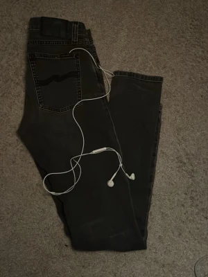 Nudie Jeans - Säljer ett par mörkt gråa skinny jeans från Nudie Jeans med klassiska bakfickor och kontrastsömmar. Jeansen har en smal passform och är tillverkade i mjukt denimtyg som sitter snyggt på benen. Extremt snygg färg för dig som vill se lite skönare ut! Skriv vid minsta fundering!                                                                       !Hörlurar tillkommer ej!