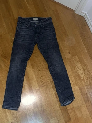 Mörkgrå slimfit jeans - Säljer ett par mörkgrå slimfit jeans med klassisk femficksdesign och diskreta slitningar. Jeansen har normal midja och raka bakfickor utan extra detaljer. Perfekta till sneakers eller boots och passar till det mesta i garderoben.