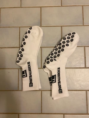 Vita FootballSocks med grepp - Ett par vita sportstrumpor från FootballSocks med svarta halkskydd under foten och logga på skaftet. Perfekta för fotboll eller annan träning där du vill ha extra grepp i skorna. Strumporna är ribbade vid skaftet och har en sportig look.