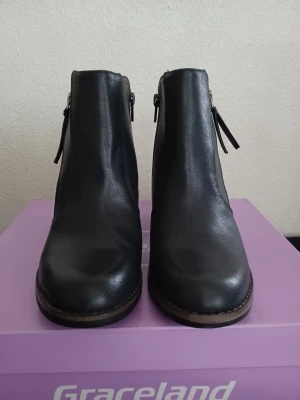 Svarta stövletter från Graceland - Snygga svarta stövletter från Graceland med rund tå och dragkedja på sidan. Skorna har en stabil hög klack och är gjorda i syntetmaterial med en stilren look. Perfekta för att lyfta din outfit med en klassisk touch. Klackhöjd:7 cm. Orginalkartong: 30×24×11. Endast provade.