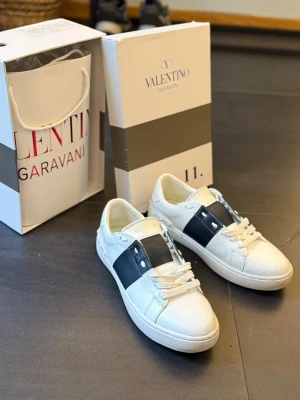 Valentino Garavani open  - Snygga vita sneakers från Valentino med bred blå detalj över mitten. Skorna har rund tå och platt sula, tillverkade i skinn för en lyxig känsla. Perfekta för dig som vill ha en stilren och exklusiv look.