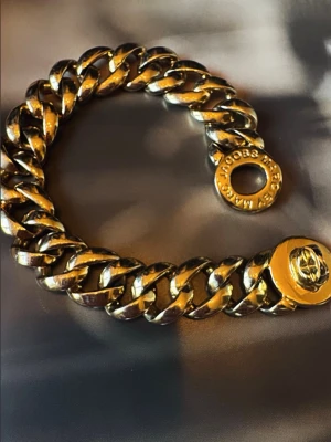  Marc Jacobs guldarmband  - Säljer ett chunky armband i guldfärgad metall från Marc Jacobs. Länkarna är breda och har en cool, glänsande finish. Låset är runt och pryds av Marc Jacobs-loggan. Perfekt statement piece för dig som gillar att sticka ut.