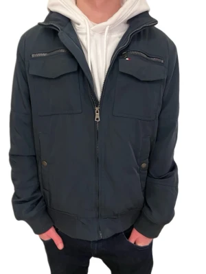 Tommy Hilfiger Multi Pocket Bomber Twilight Navy - Snygg mörkblå bomberjacka från Tommy Hilfiger med två bröstfickor med dragkedja och två sidofickor med knapp. Jackan har ribbade muddar och quiltat foder för extra värme. Sprillans ny och ej använd! 