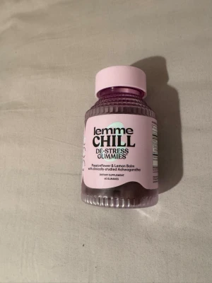Lemme Chill De-Stress Gummies - Burk med Lemme Chill De-Stress Gummies, ett kosttillskott med passionsblomma, citronmeliss och ashwagandha. Förpackningen är ljuslila med rosa lock och innehåller 60 gummies. Perfekt för dig som vill ha ett smidigt tillskott i vardagen.