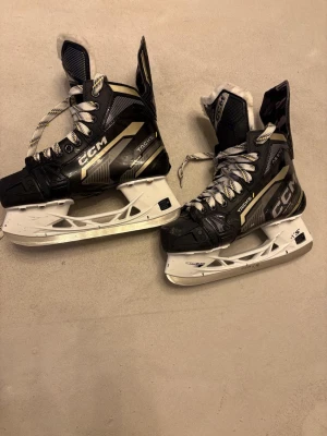 CCM Tacks 9370 hockeyskridskor - Säljer ett par svarta och vita CCM Tacks 9370 hockeyskridskor i storlek US 4 (EUR 37.5). Skridskorna har vita snören, robust plastklinga och detaljer i grått och guld. Perfekta för dig som vill ha stabilitet och bra stöd på isen.