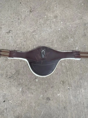 Brun magplatta med avtagbart fluff till häst - Säljer en brun magplatta i läder med avtagbart fluff, perfekt för hoppning eller träning. Passar till sadelgjord och skyddar hästens mage. Från swedish collection, nypris ca 1000.