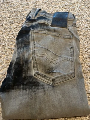 Replay Hyperflex grå jeans - Snygga Replay Hyperflex jeans i grå tvätt med svarta slitningar. Klassisk femficksmodell med bakficka och Replay-logga på läderpatch bak i midjan. Jeansen har en modern passform och är tillverkade i stretchigt jeansmaterial för extra komfort.