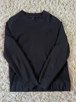 Svart basic tröja med struktur - En stilren svart tröja i mycket gott skick med diskret strukturmönster på framsidan och släta ärmar. Tröjan har rund halsringning och ribbade muddar vid ärmslut och nederkant. Perfekt för en clean och enkel look. Storlek L men passar även M (jag brukar har M)
