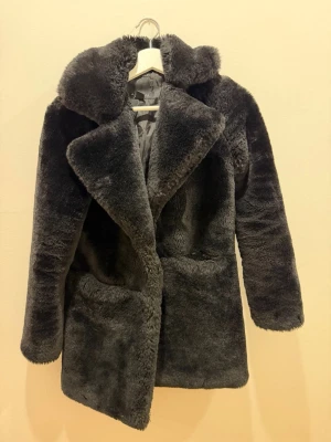 Svart pälsjacka med bred krage - Svart pälsjacka med bred krage och lång ärm. Jackan har en oversized look och är gjord i mjuk fuskpäls som ger en lyxig känsla. Perfekt för kalla dagar när du vill vara både varm och trendig.