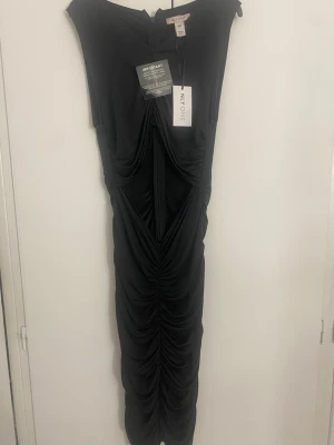 Svart midiklänning från NLY One - Snygg svart midiklänning från NLY One med draperad design och cut out-detalj framtill. Klänningen har figurnära passform, rund halsringning och är ärmlös. Materialet är stretchigt och följsamt, perfekt för en trendig look.Aldirg använd 