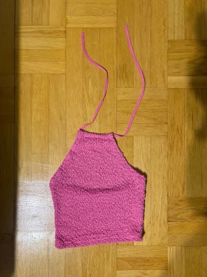 Rosa croppad linnetopp - Trendig rosa croppad linnetopp med knytband i nacken. Toppen är ärmlös och har en strukturerad, lätt skrynklig yta som ger en cool look. Perfekt för varma dagar och snygg att styla med jeans eller kjol.