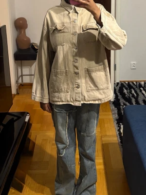 Beige oversized jeansjacka - Säljer en beige oversized jeansjacka med stora fickor fram och knappstängning. Jackan har klassisk krage, raka ärmar och coola sömdetaljer. Perfekt för dig som gillar en avslappnad och trendig stil. 
