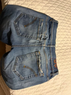 Dondup - Ljusblå jeans med raka ben och klassisk femficksdesign. Jeansen har slitna detaljer på ena bakfickan och kontrastsömmar. Tillverkade i jeanstyg med en avslappnad passform och midwaist.