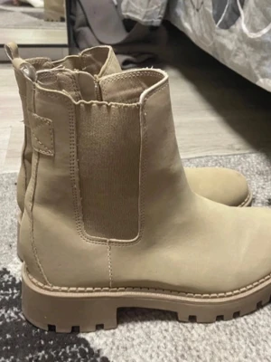 Beige chelsea boots i skinn - Snygga beige chelsea boots med grov sula och elastiska paneler på sidorna. Tillverkade i slätt skinn med rund tå och klassisk siluett. Perfekta för dig som vill ha en stilren och trendig look.