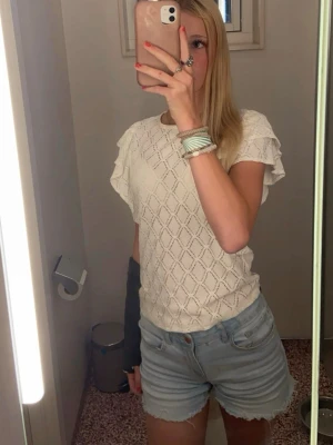 Vit stickad blus med mönster - Säljer en vit stickad topp med korta ärmar och ett snyggt tmönster. Toppen har en avslappnad passform och är perfekt att matcha med jeansshorts eller kjol. Materialet känns mjukt och luftigt, perfekt för varmare dagar, då den också är lite genomskinlig.