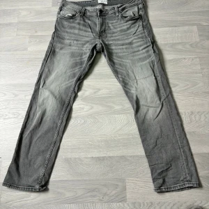 Grå Levi's 501 straight jeans - Säljer ett par grå Levi's 501 jeans med klassisk rak passform och femficksmodell. Jeansen har slitningar och tvättade detaljer för en cool, avslappnad look. Tillverkade i bomull med knappgylf och normal midja.