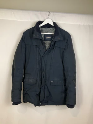 Herno Jacka - Tja säljer en snygg mörkblå jacka från Herno med krage och detaljer som dragkedjor och knappar framtill. Jackan är i väldigt fint skick och säljs för endast 1599kr. Nypris över 7000kr. Skriv vid frågor eller ifall du vill ha fler bilder. Storlek Small.