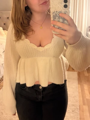 Vit stickad topp med volangkant - Säljer en söt vit stickad topp med volangkant och djup urringning. Tröjan har långa, vida ärmar och en figurnära passform upptill som blir lösare nedtill. Perfekt för dig som gillar trendiga och feminina plagg. Tröjan är originellt från Shein och har dessvärre tappat dem snören som ska sitta framåt. 💞