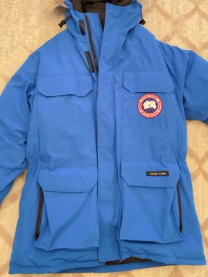  Canada Goose vinterjacka  - Snygg äkta blå parkajacka från Canada Goose med klassisk logga på bröstet. Jackan har flera stora fickor framtill, hög krage och dragkedja med vindslå. Perfekt för kalla dagar och har en riktigt clean look. Den är i princip nyskick och är knappt använd. Storlek M.
