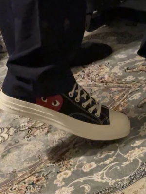 Converse x CDG Play svarta sneakers - Svarta Converse x Comme des Garçons Play sneakers med den ikoniska röda hjärtloggan på sidan. Skorna har vita snören, kontrastsömmar och en tjock vit gummisula. Klassisk rund tå och lågt skaft för en clean och stilren look.