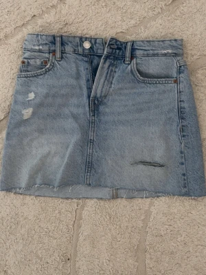 Ljusblå jeanskjol  - Ljusblå jeanskjol med slitningar, för liten för mig men sitter annars low/mid waist. Midjemåttet: 36cm längd: 33cm. Aldrig använd