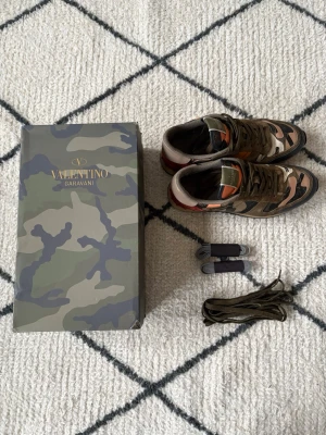 Valentino skor - Säljer ett par Valentino Garavani Rockrunner sneakers storlek 43 i camomönster med inslag av grönt, beige, svart, orange och vinrött. Skorna har detaljer i mocka, skinn och textil samt klassisk snörning. Kommer med originalkartong och extra skosnören.