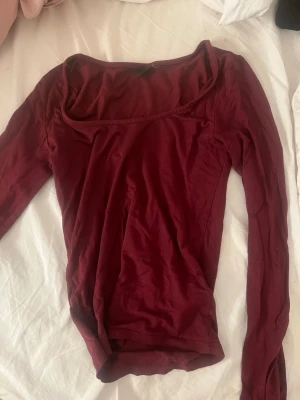 Mörkröd långärmad topp - Snygg mörkröd långärmad topp med bred, fyrkantig ringning. Tillverkad i mjukt bomullsmaterial som sitter skönt mot kroppen. Perfekt att styla med jeans eller kjol för en trendig look.