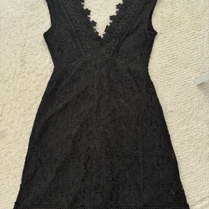 Svart spetsklänning från Bik Bok XS - Supersnygg svart kort klänning från Bik Bok i spets med blommiga detaljer och djup v-ringning. Ärmlös modell med figurnära passform. Yttermaterialet är en mix av polyamid och bomull, fodret är i polyester. Perfekt för dig som vill sticka ut med en elegant look.