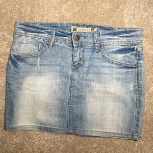 Blå jeanskjol med fickor, strl 36 - Snygg ljusblå jeanskjol i klassisk femficksmodell med slitningar och detaljerade sömmar. Kjolen har knapp och dragkedja framtill samt bälteshällor. Passar dig som gillar en chill och avslappnad stil. Längd 32 cm, midja 24 cm, gylf 10 cm